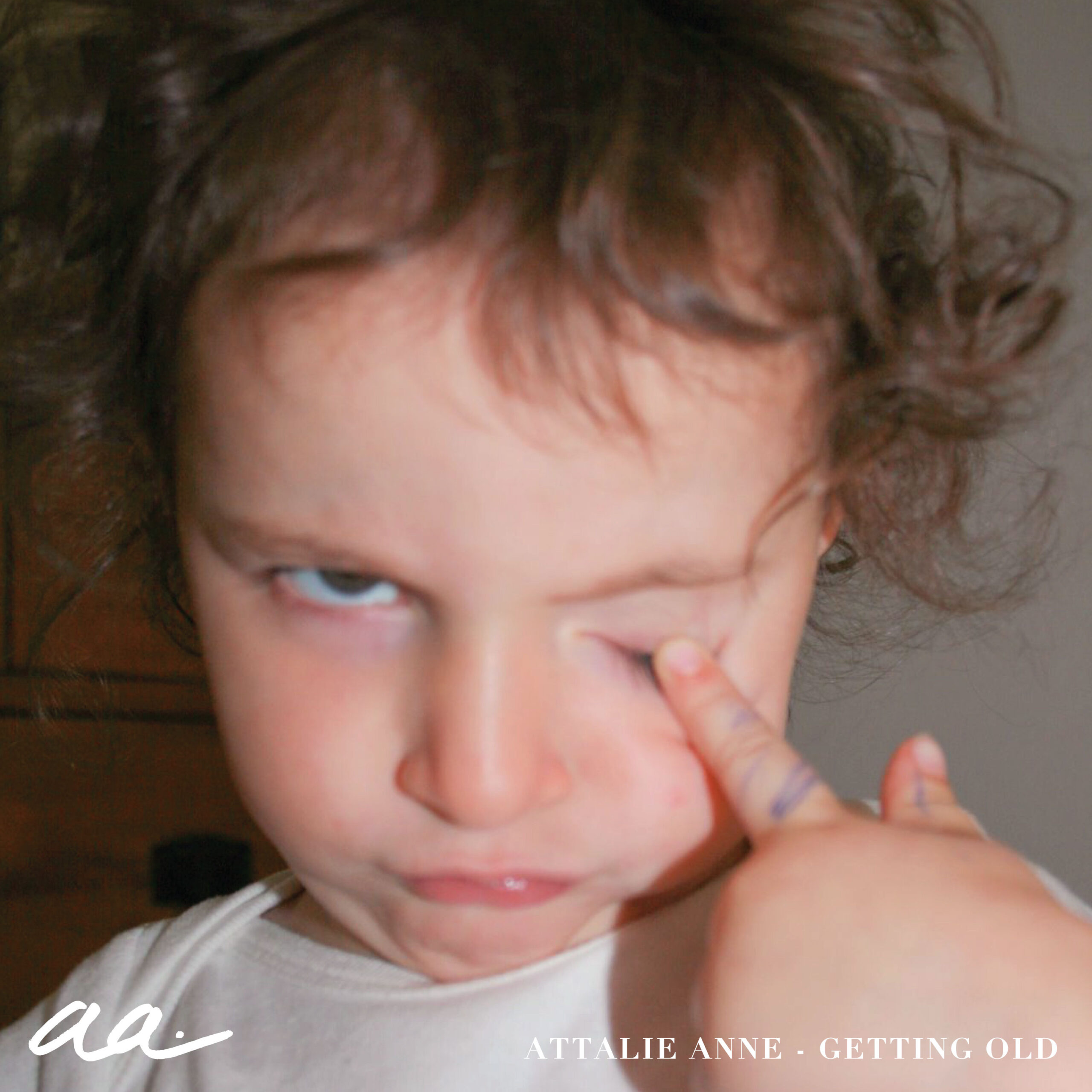 Attalie Anne’s “getting old” cover art. A photo of toddler Attalie frowning and poking her left eye. There is pen marks on her finger from where she drew on herself.
